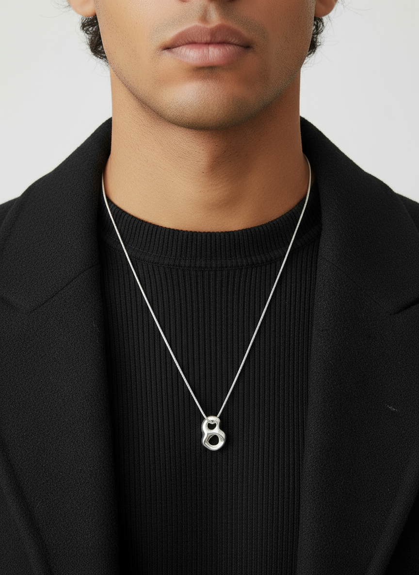 Man wearing a silver necklace with a pendant against a neutral background