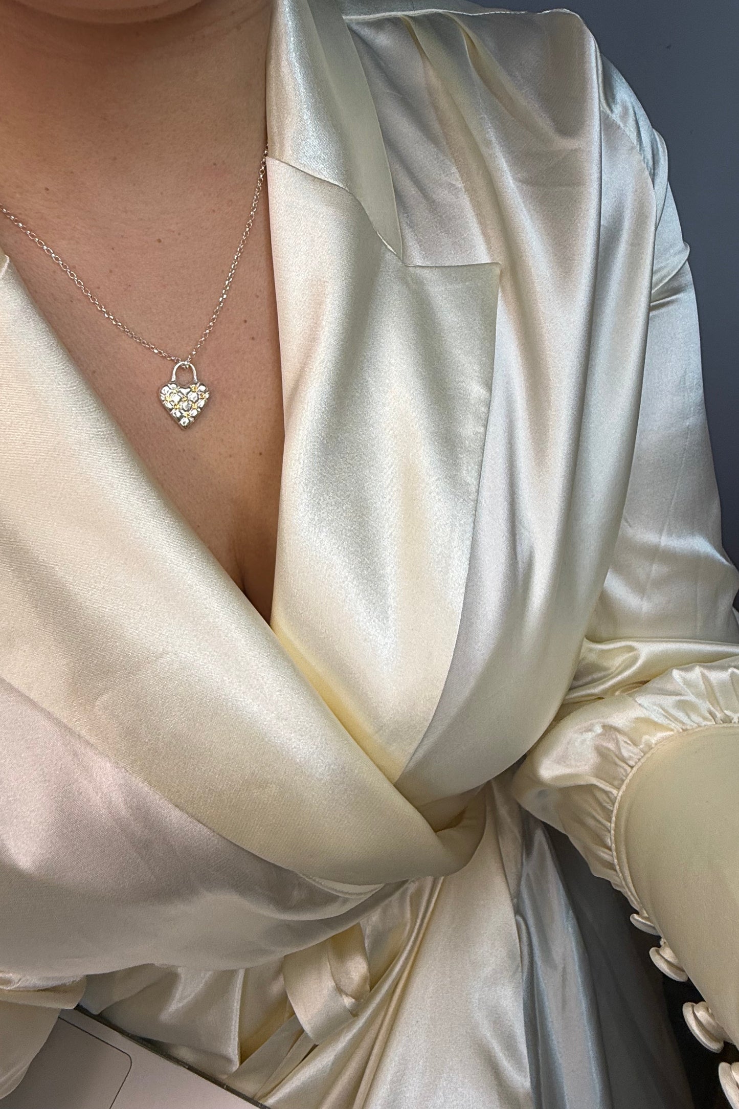 Close-up of a person wearing a white satin dress with a heart-shaped necklace. The heart in the necklace has a cushioned effect and has 7 yellow sapphires at the intersections.