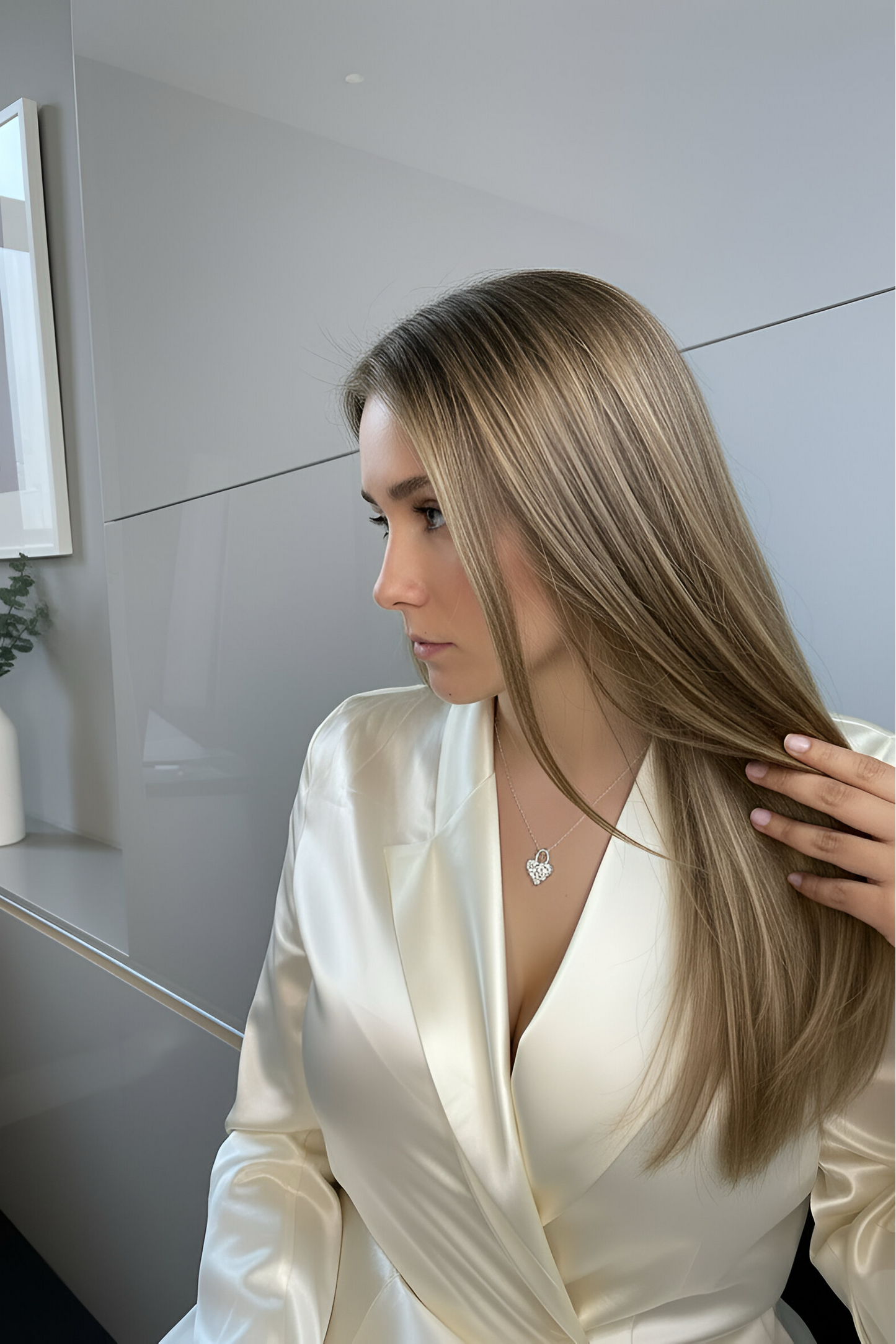 A woman in a white satin dress sitting indoors. She is wearing a heart-shaped lock necklace, cushioned heart with 7 white moissanites at each intersection.
