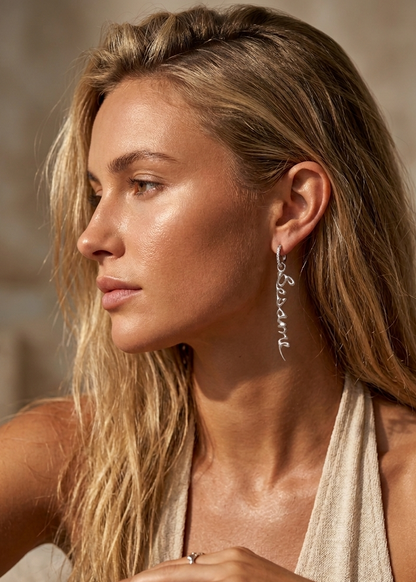 Woman wearing silver earrings with the script "Besame Mucho" with a neutral background