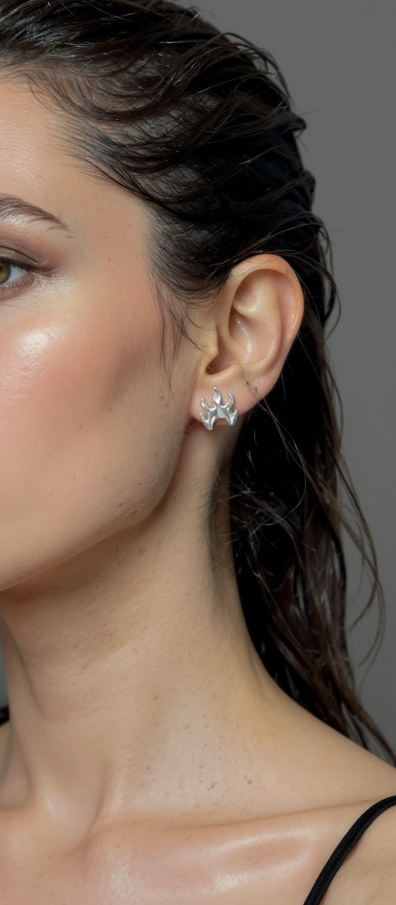 Close-up of a woman wearing a silver flame earring against a neutral background