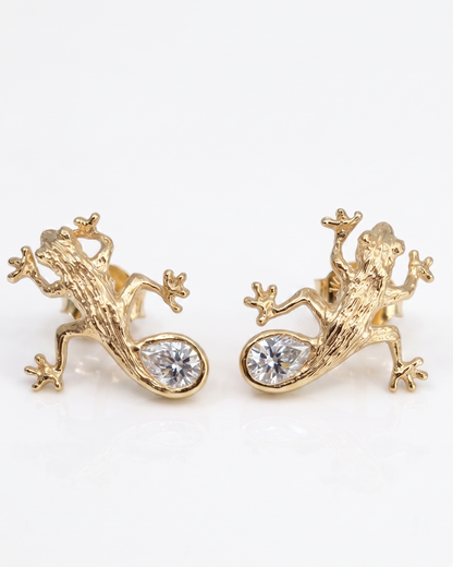 Luxury Solid sterling silver gecko-shaped earrings, 14K gold-plated, with a pear-shaped white moissanite stone. The earring is crafted by hand and showcased on a cactus plant.