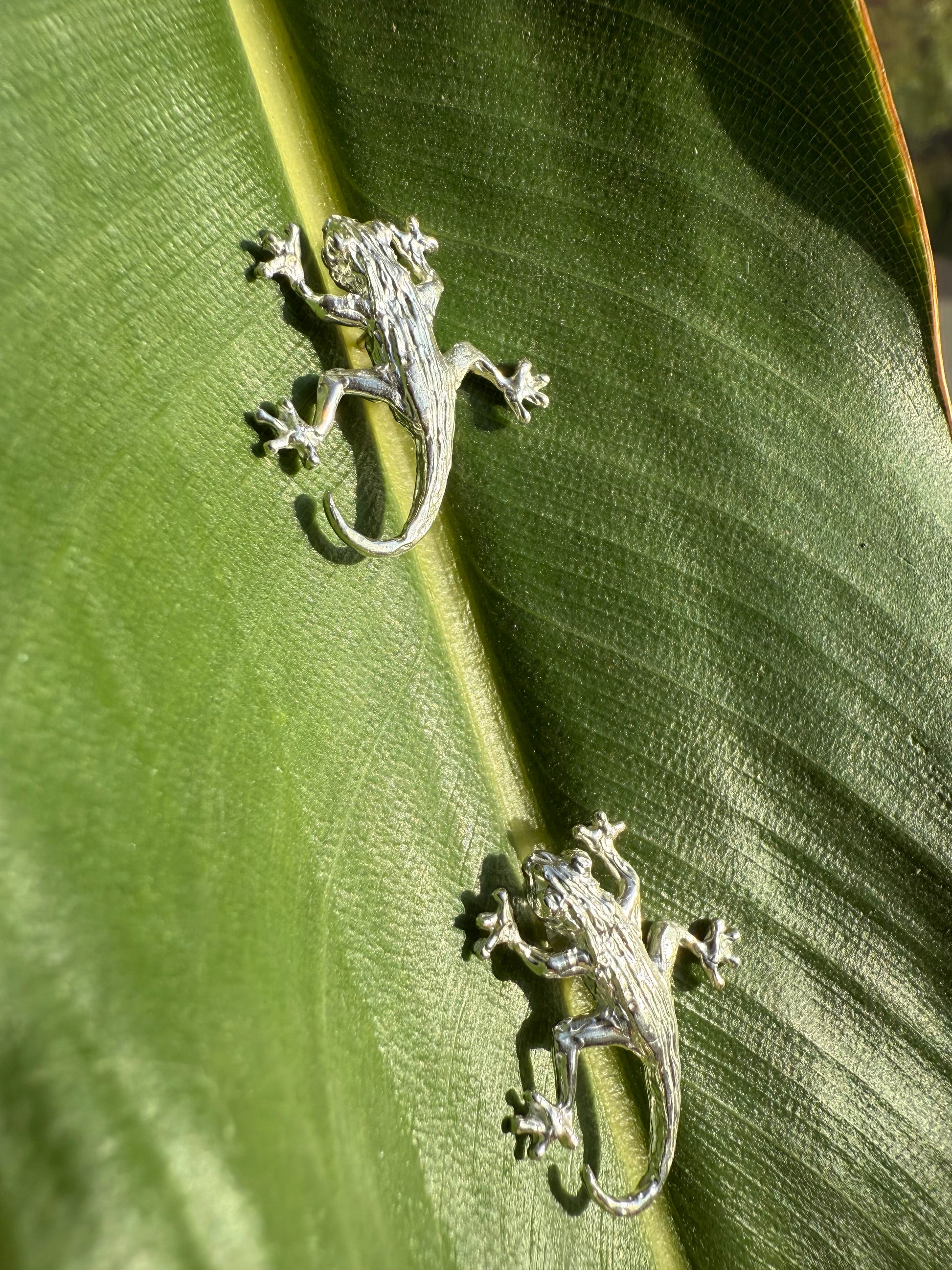 Two silver lizard-shaped earrings on a green leaf