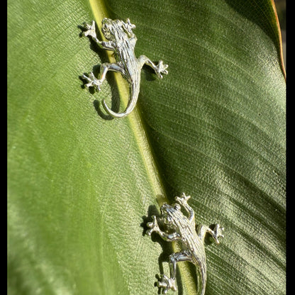 Two silver lizard-shaped earrings on a green leaf