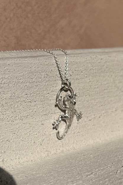 Silver gecko-shaped pendant on a chain against a neutral background
