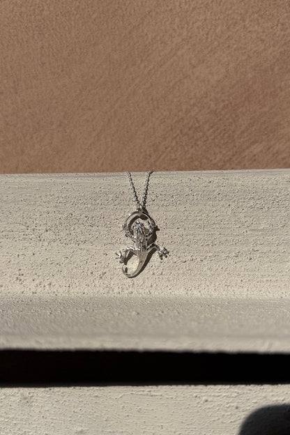 Silver Gecko pendant on a chain against a beige background
