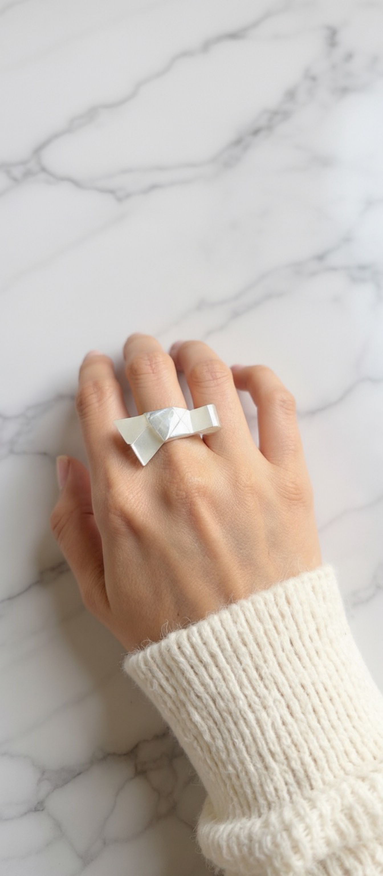Hand wearing a white bow ring on a marble surface