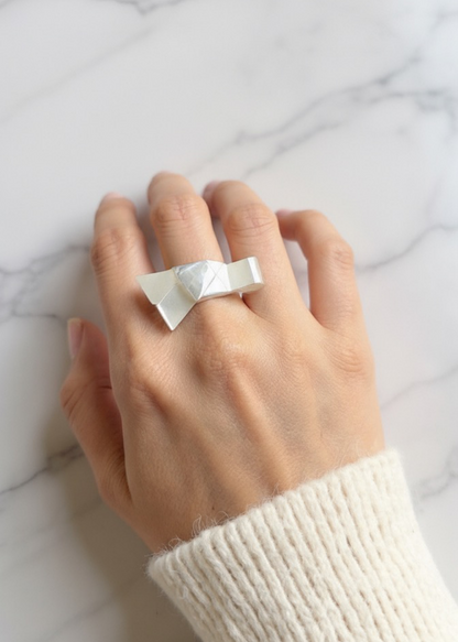 Hand wearing a white bow ring on a marble surface