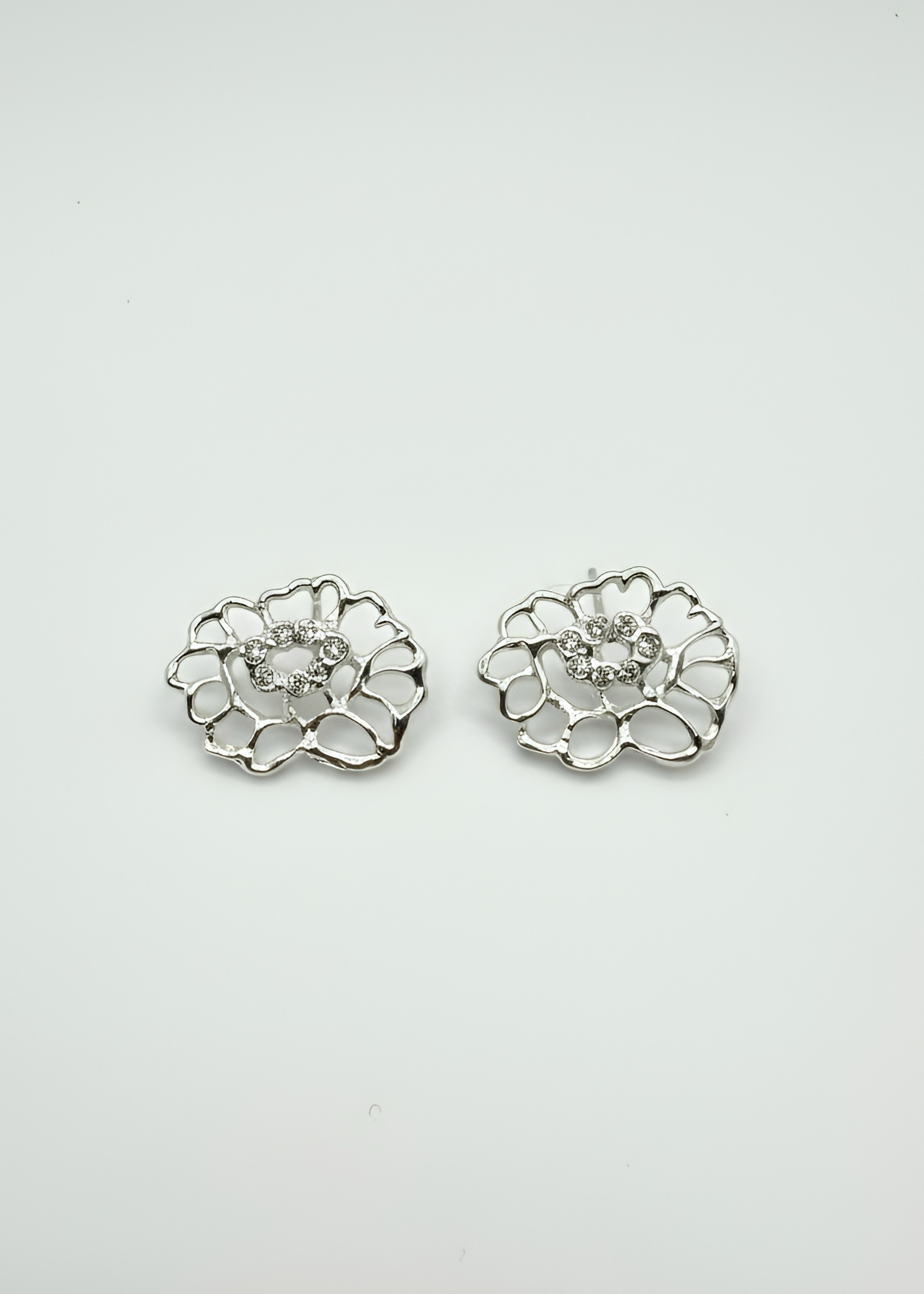 A pair of silver-toned lace flower-shaped stud earrings with a clear central gemstone, displayed on a clean white background.
