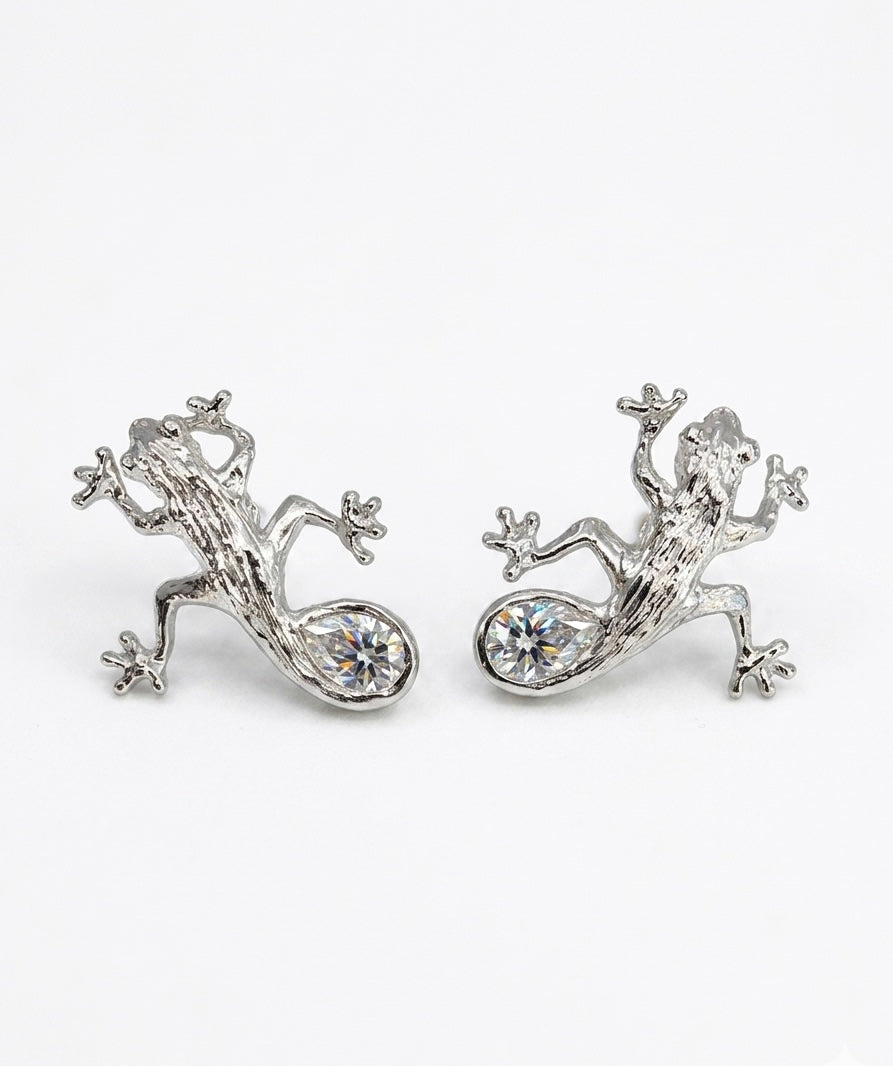 Luxury Solid sterling silver gecko-shaped earrings with a pear-shaped white moissanite stone. The earring is crafted by hand and showcased on a cactus plant.