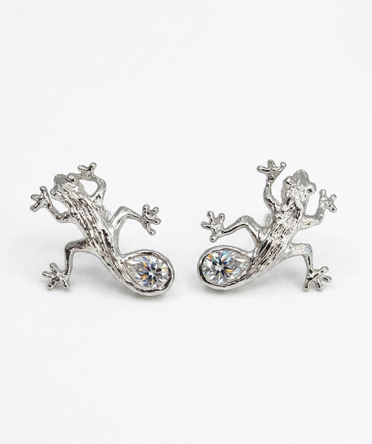 Luxury Solid sterling silver gecko-shaped earrings with a pear-shaped white moissanite stone. The earring is crafted by hand and showcased on a cactus plant.
