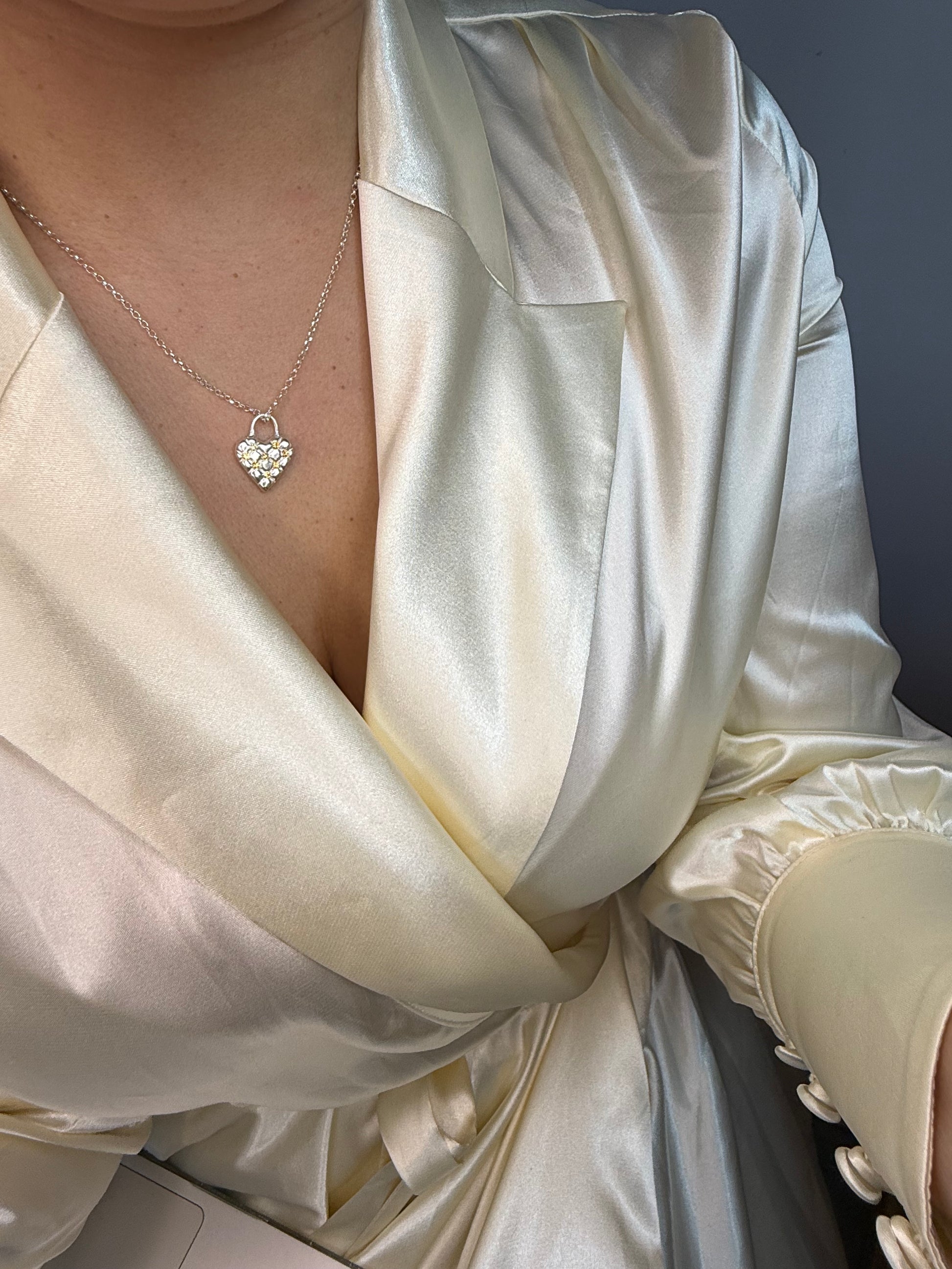 Close-up of a person wearing a white satin dress with a heart-shaped necklace. The heart in the necklace has a cushioned effect and has 7 yellow sapphires at the intersections.