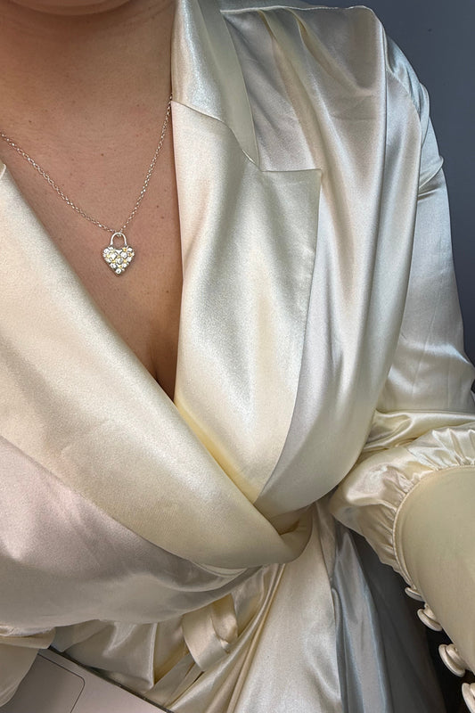 Close-up of a person wearing a white satin dress with a heart-shaped necklace. The heart in the necklace has a cushioned effect and has 7 yellow sapphires at the intersections.