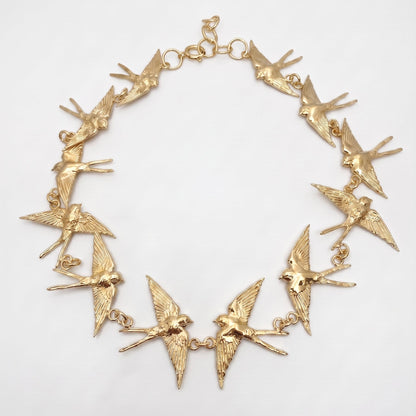 A gold-tone statement necklace featuring multiple dangling swallow bird charms connected by small chain links, displayed on a clean white background.