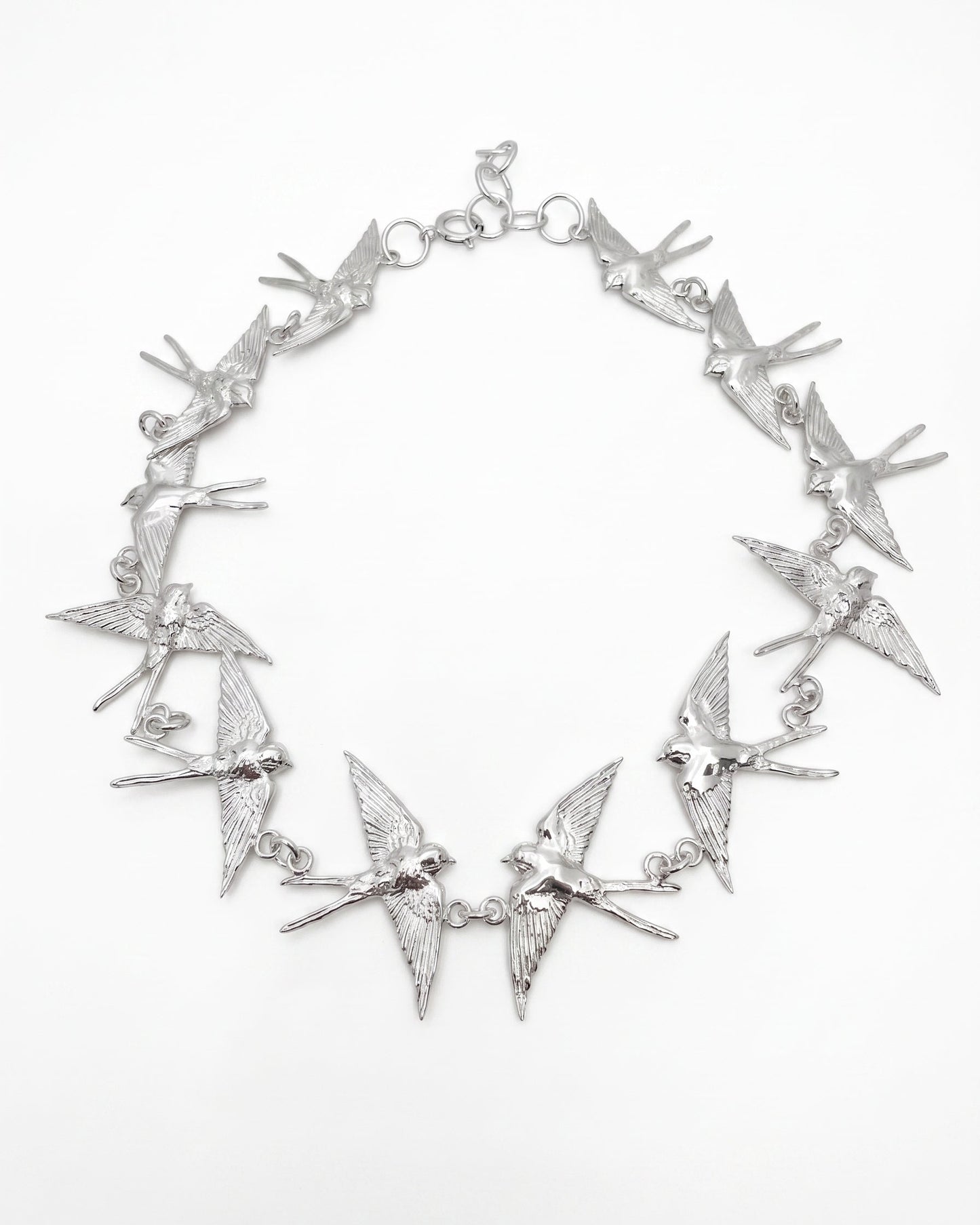 An sterling silver statement necklace featuring multiple dangling barn swallows  arranged in a circle on a plain white background.