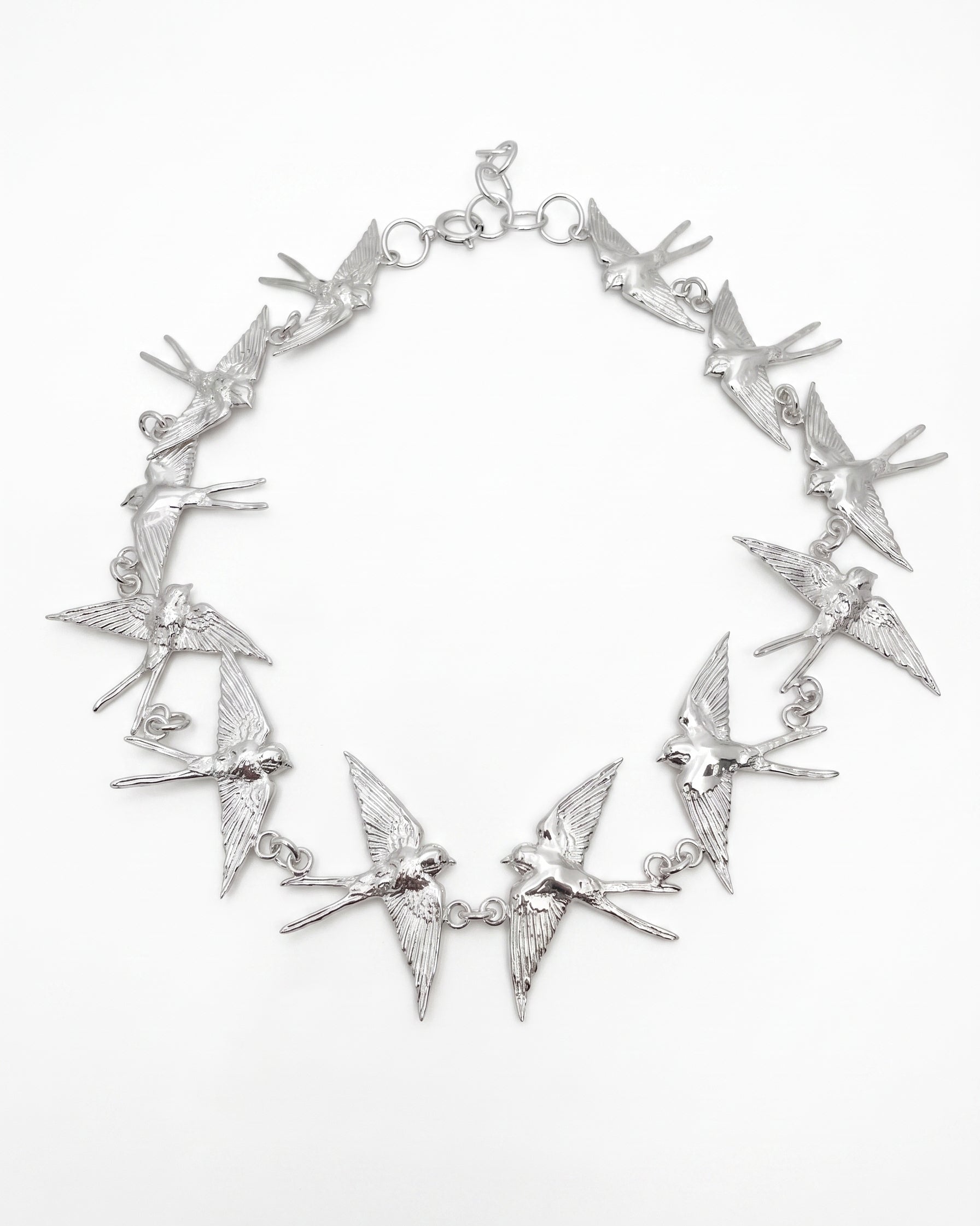 An sterling silver statement necklace featuring multiple dangling barn swallows  arranged in a circle on a plain white background.