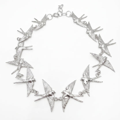 An sterling silver statement necklace featuring multiple dangling barn swallows  arranged in a circle on a plain white background.