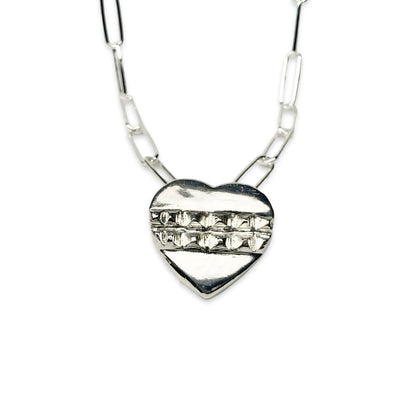 A silver pendant in the shape of a heart with a textured surface and a chain attached to it.