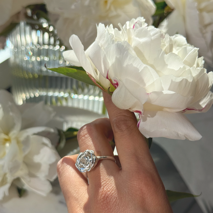 Hand holding white flowers with a silver rose ring on a blurred background