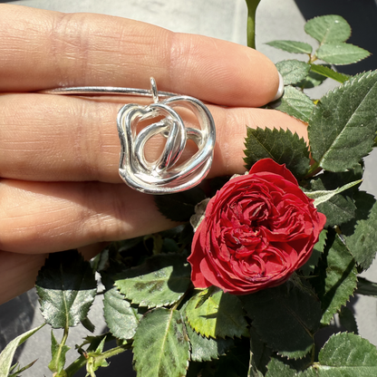 Silver rose-shaped pendant held by a hand with a red rose and green leaves in the background