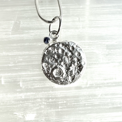 Silver and sapphire moon pendant necklace on a textured white background